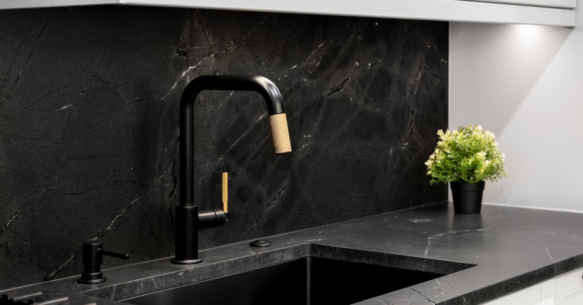 A close-up of a black sink in a kitchen with white cabinets. Black quartz counters and backsplash surround the sink.