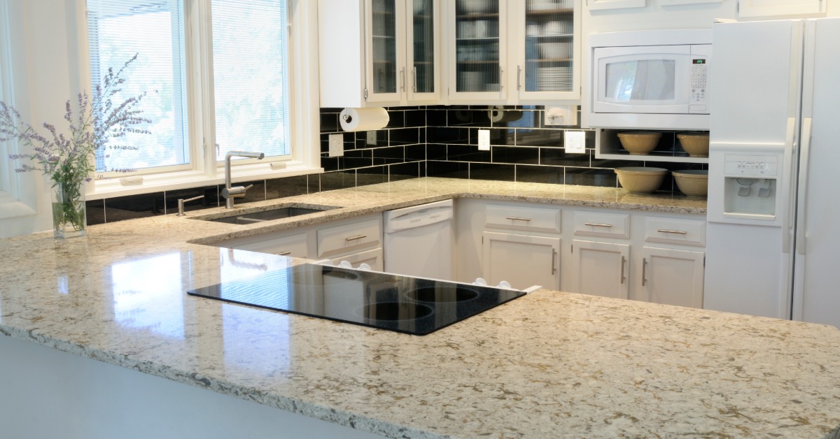 A large kitchen with quartz countertops in a neutral tone of whites and greys. The backsplash is made from a black subway tile.