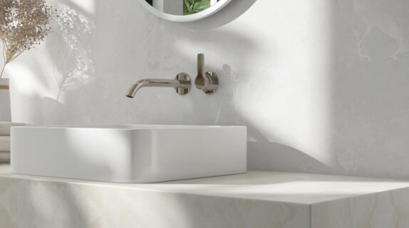 A close-up of a creamy, white marble bathroom countertop. A square porcelain sink rests on top of the counter.