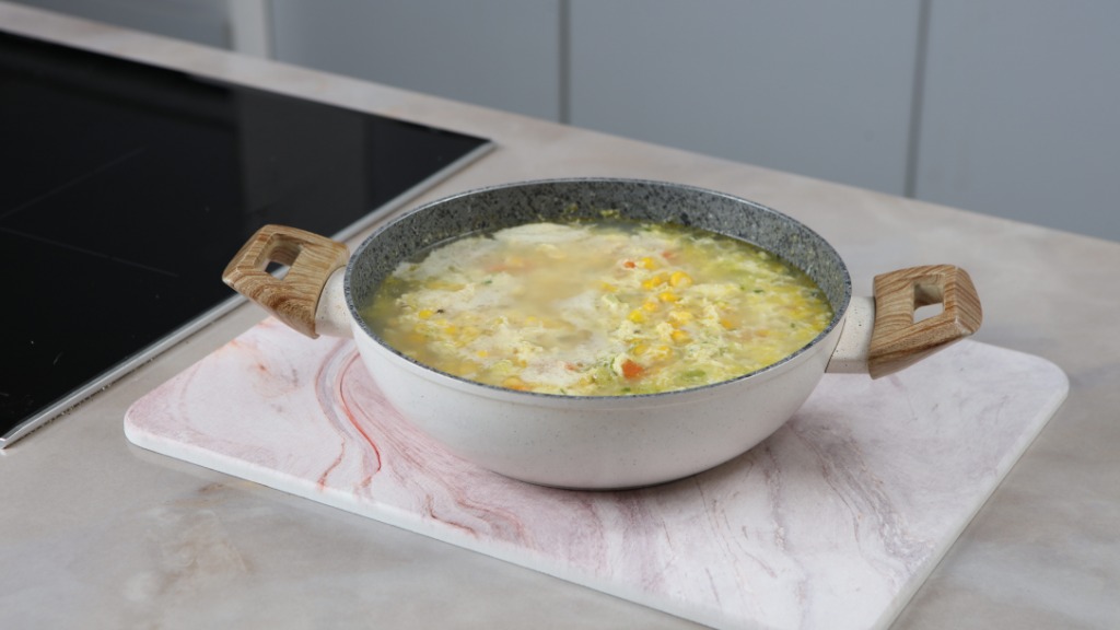 A close-up of a large pot of soup with wooden handles. The pot rests on a trivet on top of a countertop.