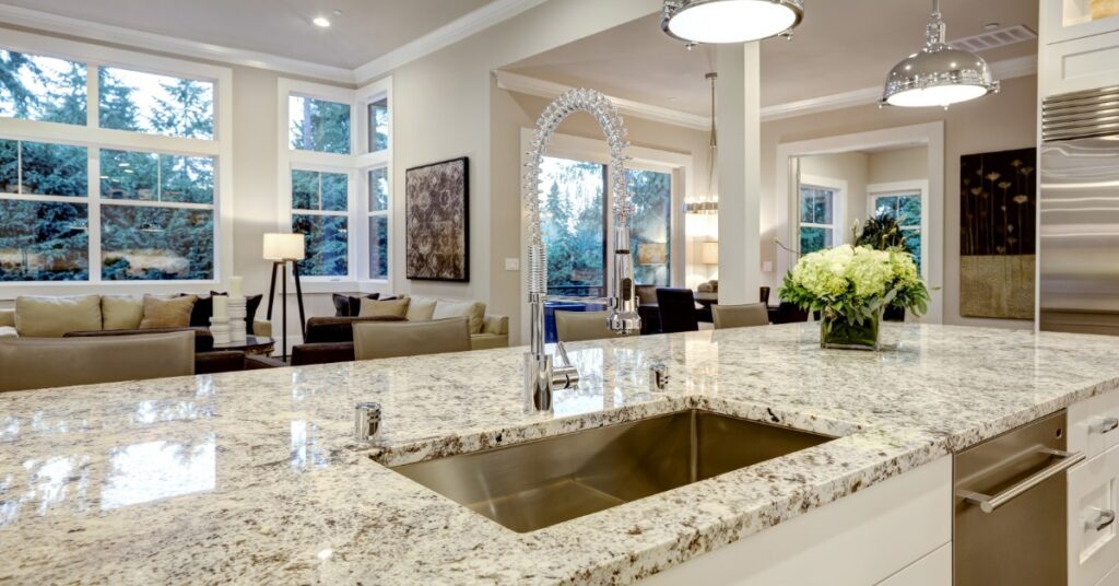 A white kitchen with a silver sink in a modern home. The countertops are a black and white granite material.